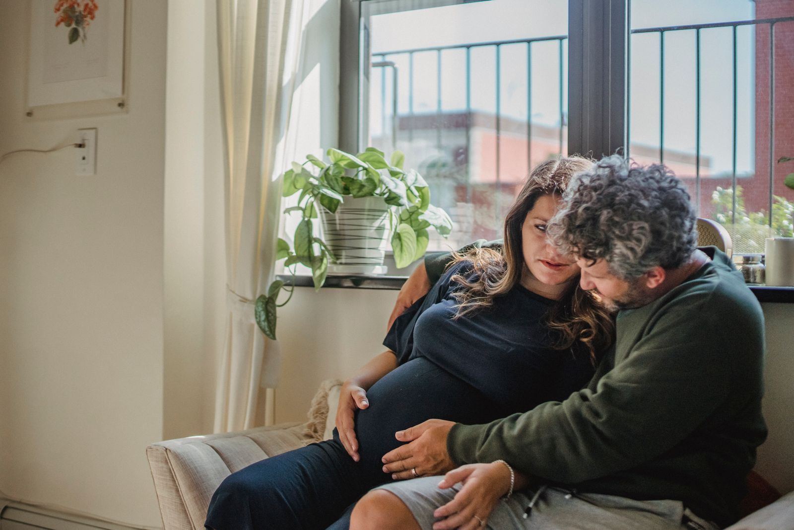 Mãos entrelaçadas repousando sobre uma barriga grávida em luz suave
