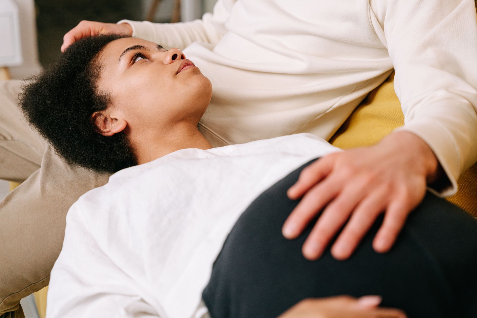 Mãos entrelaçadas repousando sobre uma barriga grávida em luz suave